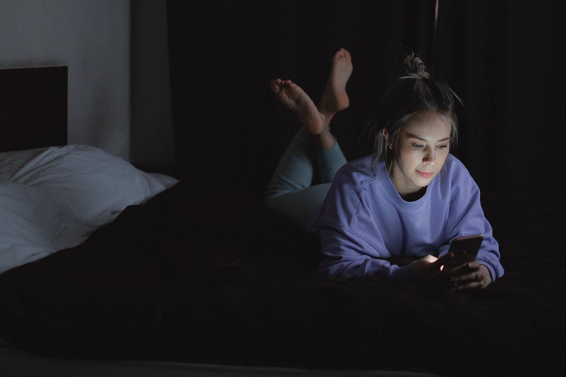 woman lying on bed while using a cellphone
